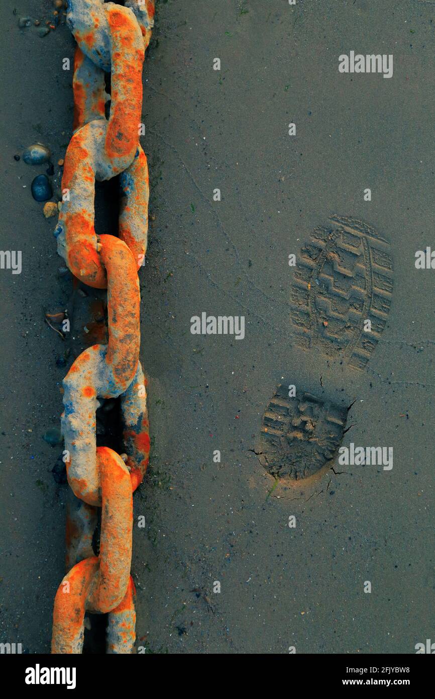 Footprint on the sand next to corroded chain Stock Photo