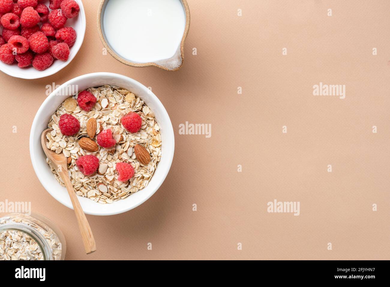 Uncooked dry oats muesli with nuts and berries in bowl and almond milk in jug on beige background, top view, copy space Stock Photo