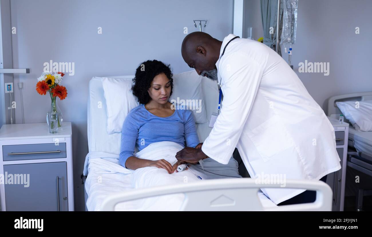 African american male doctor putting pulse oximeter on finger of mixed