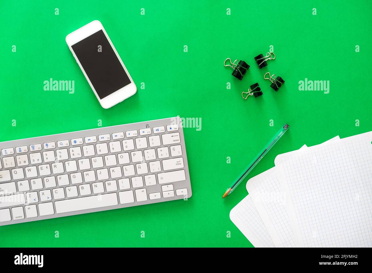 mobile phone, wireless keyboard, pen, papers and clips on green background Stock Photo
