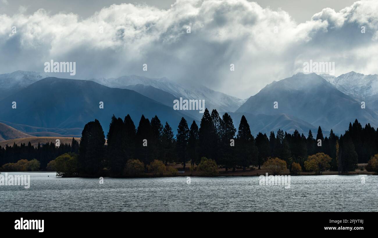 Stormy clouds over Ben Ohau Range with trees in silhouette and lake ...