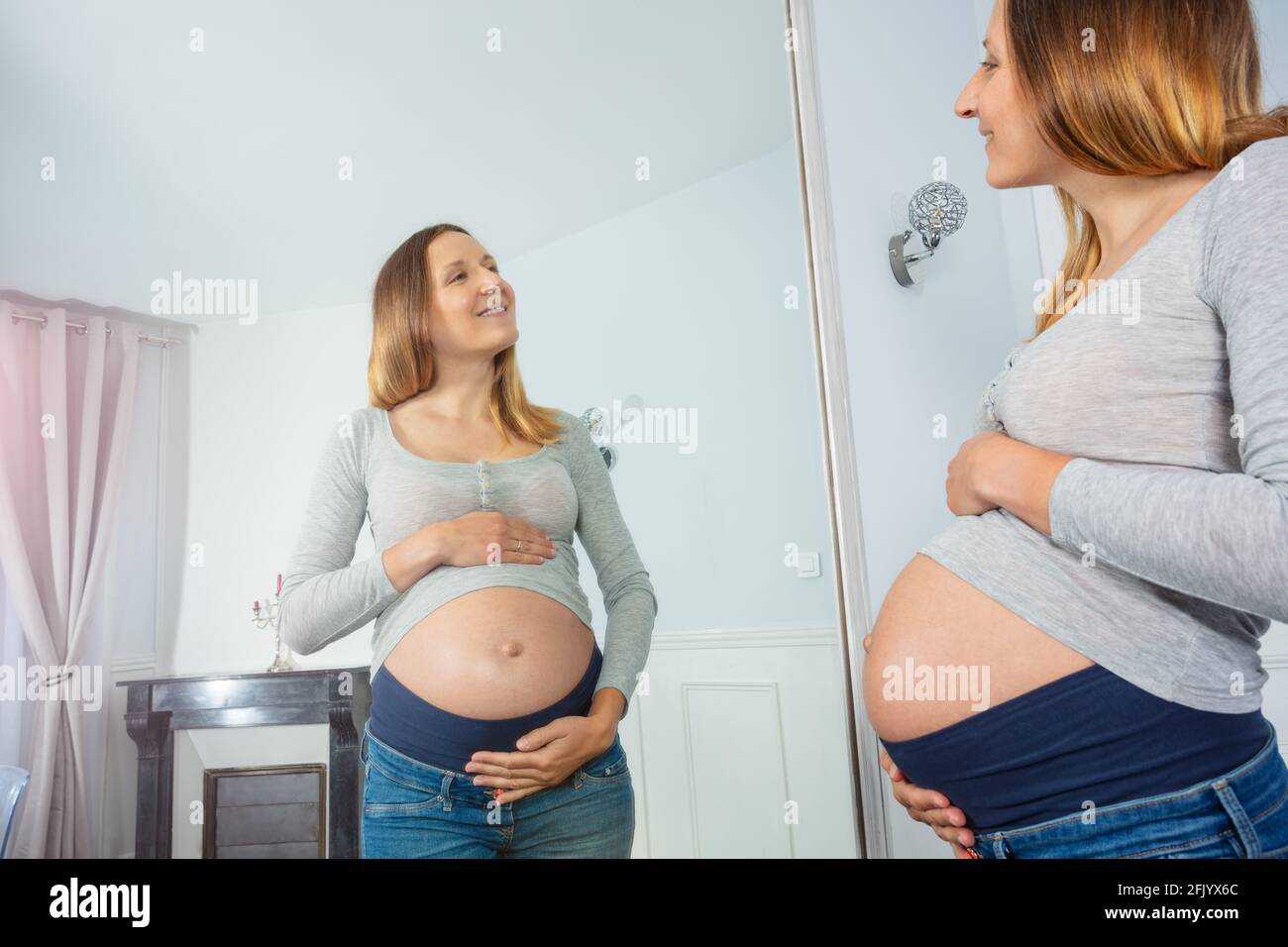 Happy pregnant woman pose near the mirror smiling Stock Photo