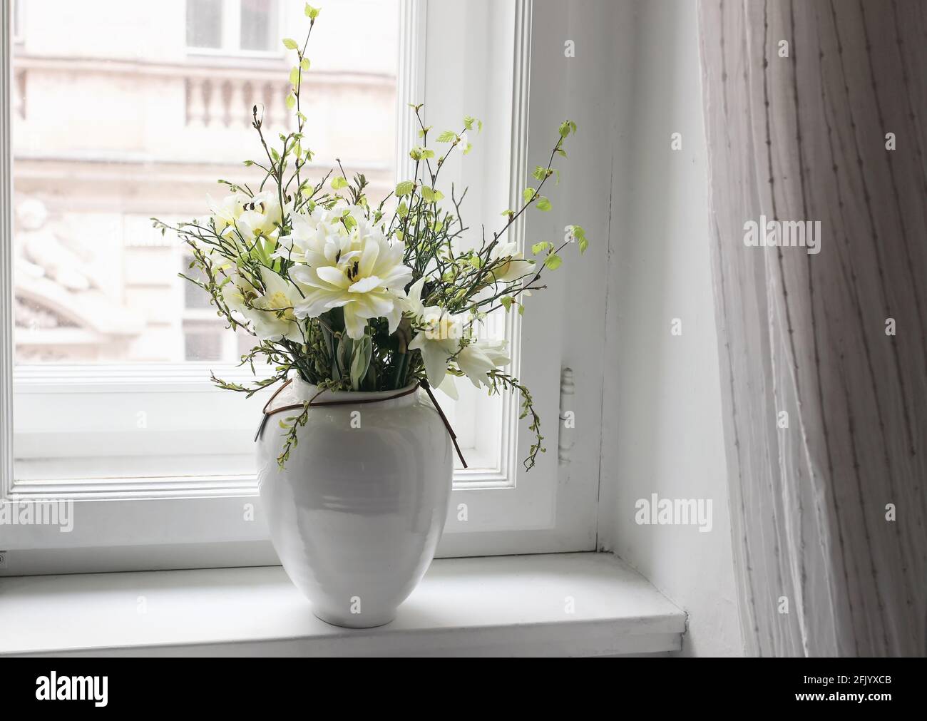 Easter spring still life. Floral bouquet on window sill. White and yellow tulips, daffodils flowers and green birch tree and blueberry branches in Stock Photo