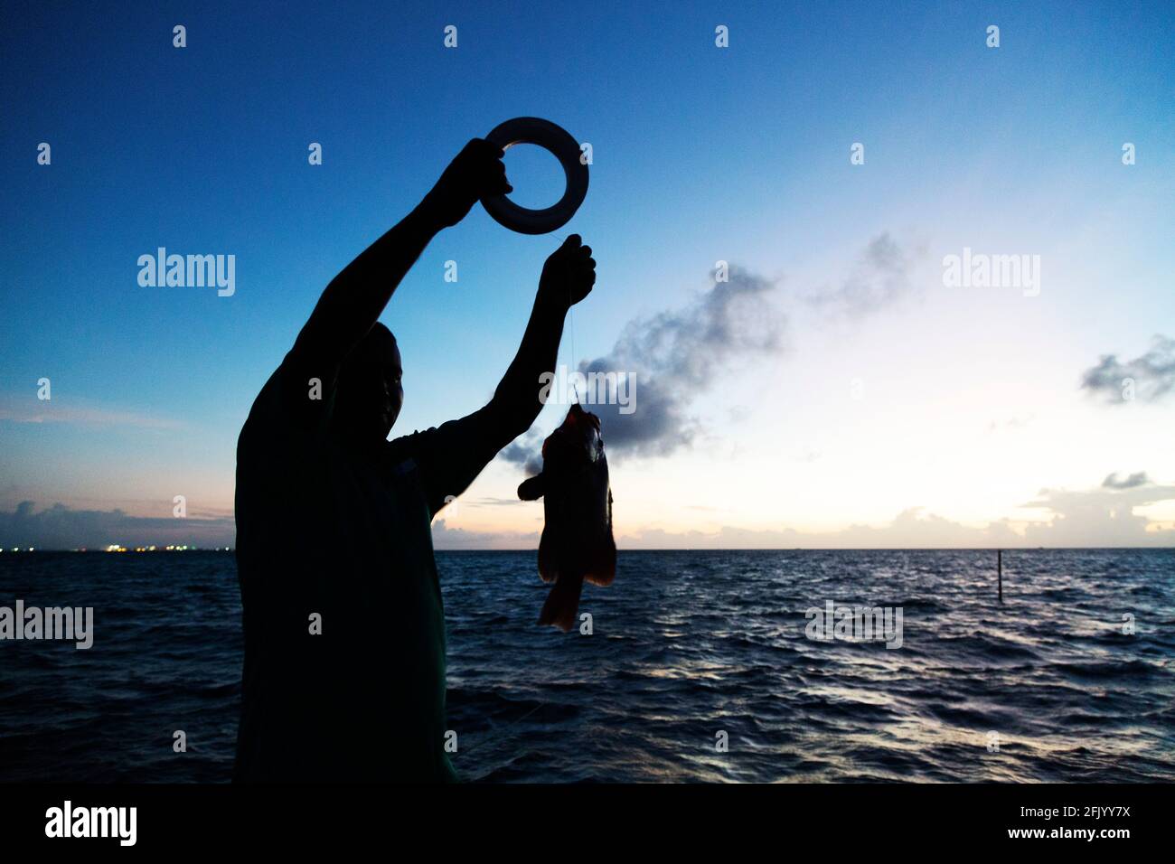 Fisherman holds up a fish caught during a night fishing trip in the Maldives. The fish has been caught on a line using a reel. Stock Photo