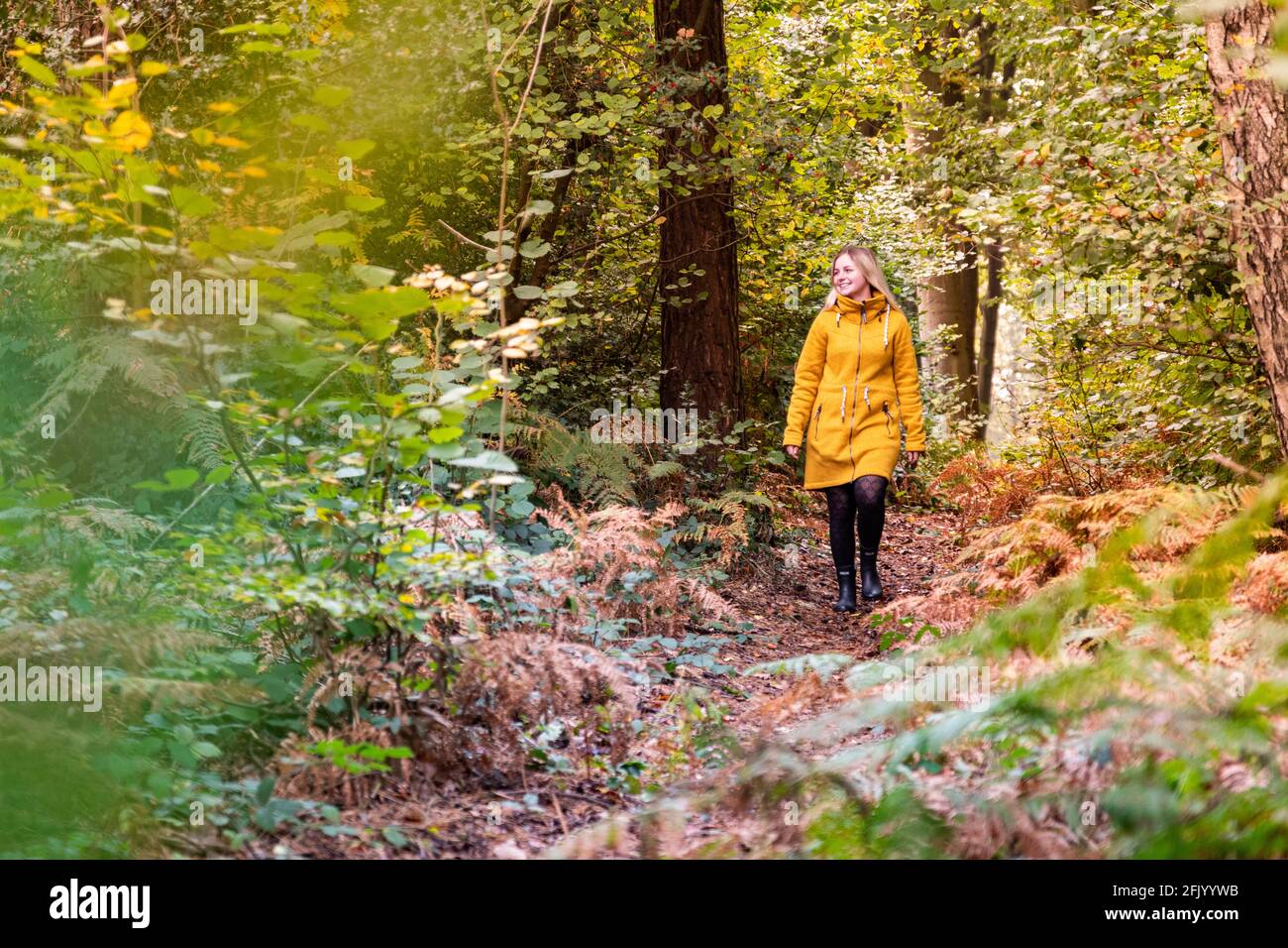 Blonde woman in yellow jacket walking through a forest clearing ...