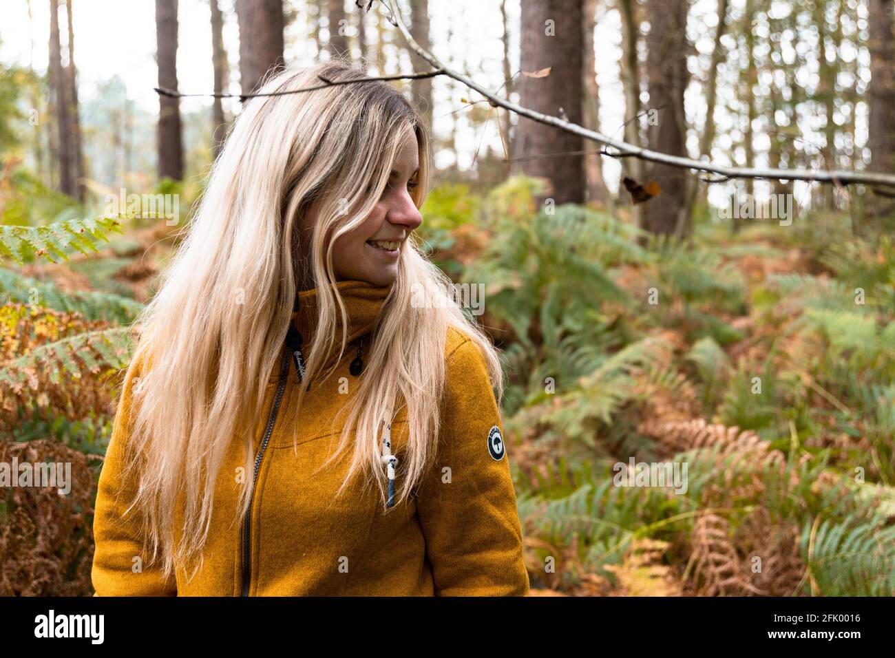 Blonde woman in yellow jacket walking through a forest clearing ...