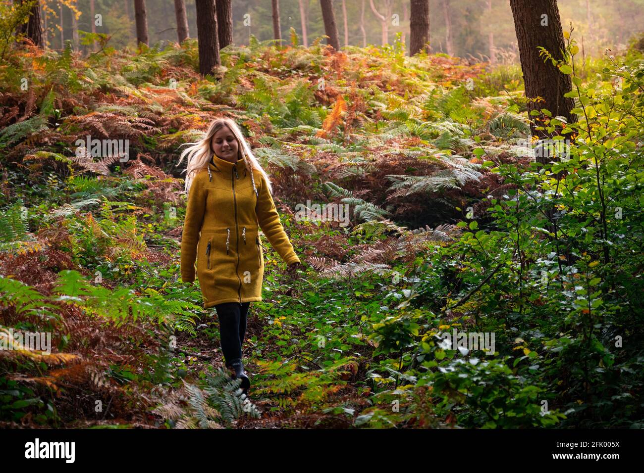Blonde woman in yellow jacket walking through a forest clearing ...