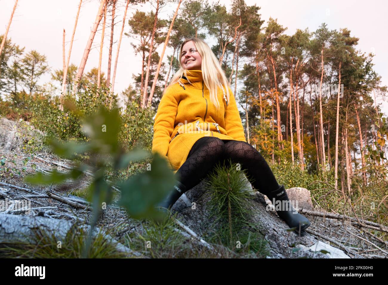 Blonde woman in yellow coat sitting in the autumn forrest. Relaxing in ...