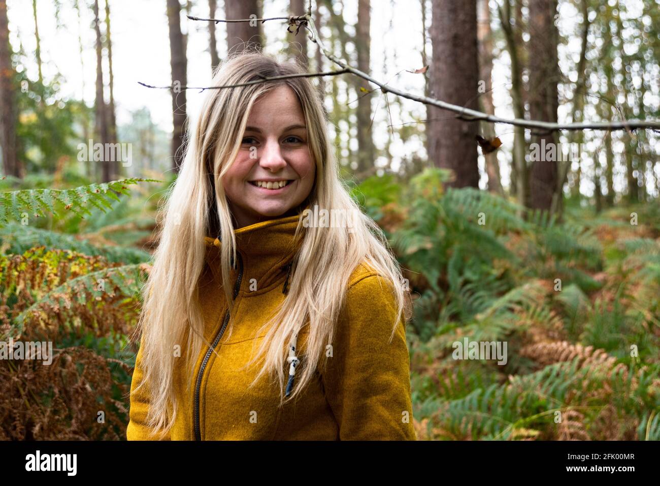 Blonde woman in yellow jacket walking through a forest clearing ...