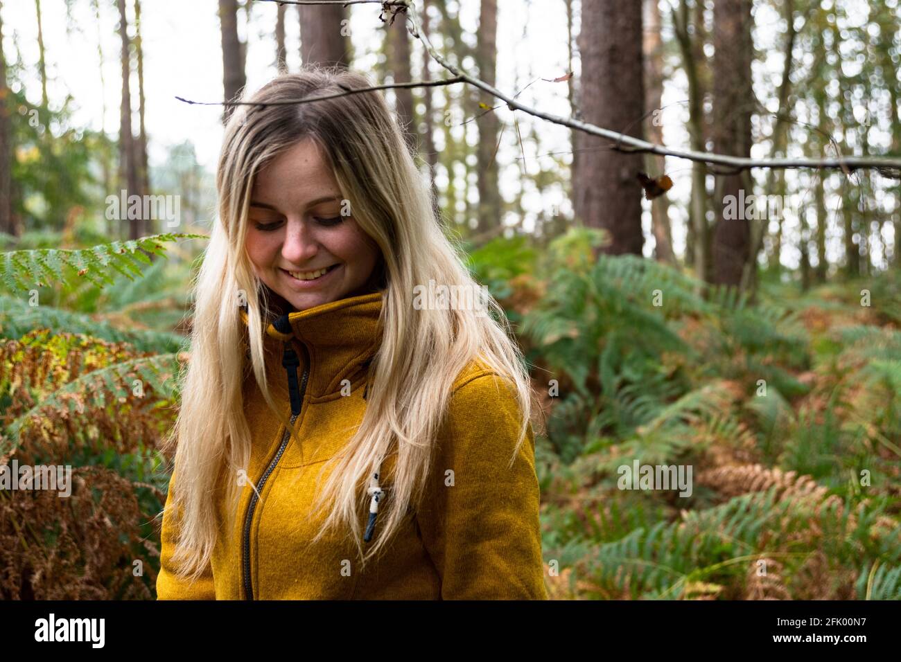 Blonde woman in yellow jacket walking through a forest clearing ...