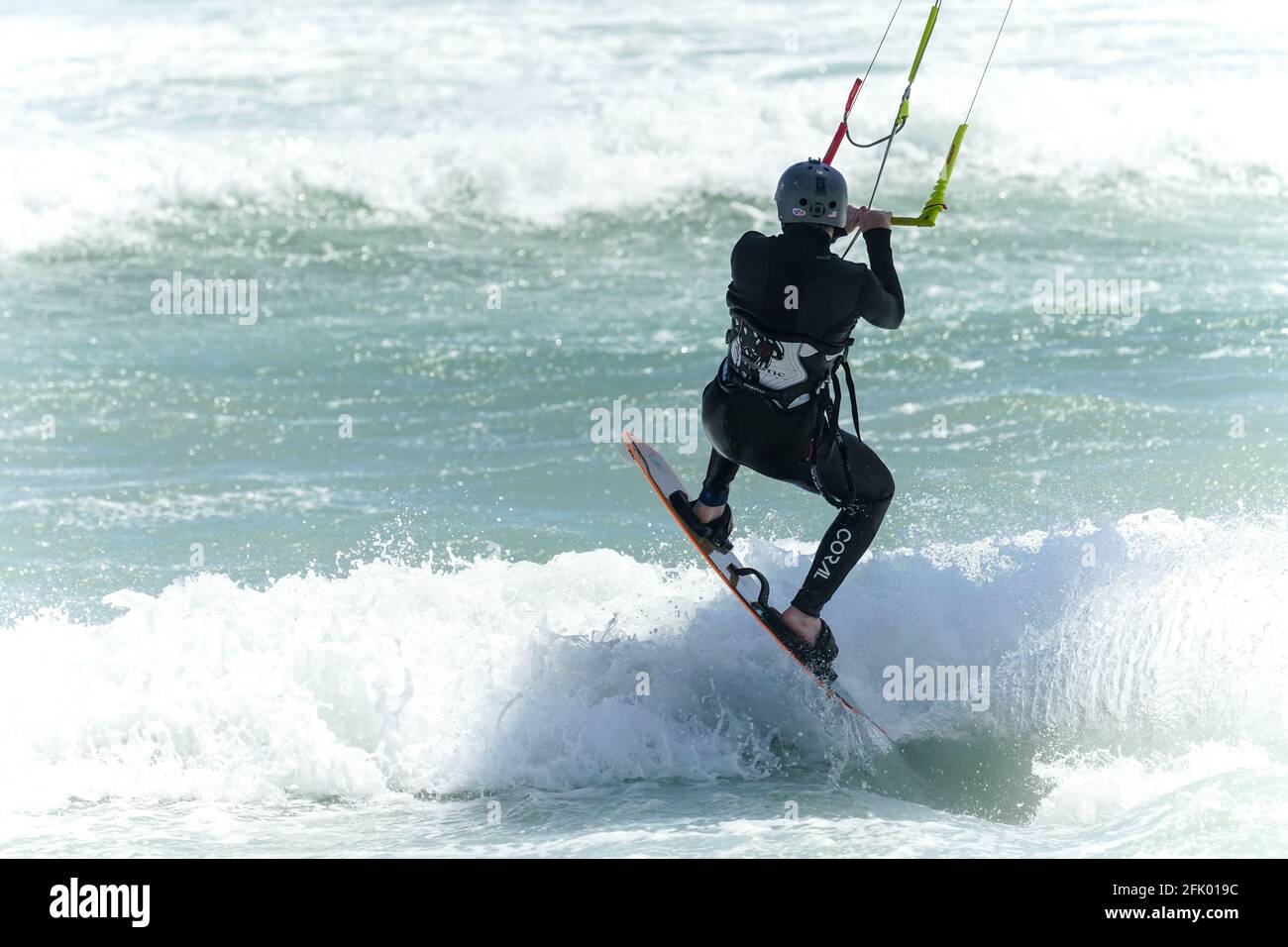 kite surfer or kite boarder holds onto a harness and jumps a wave on the ocean Stock Photo