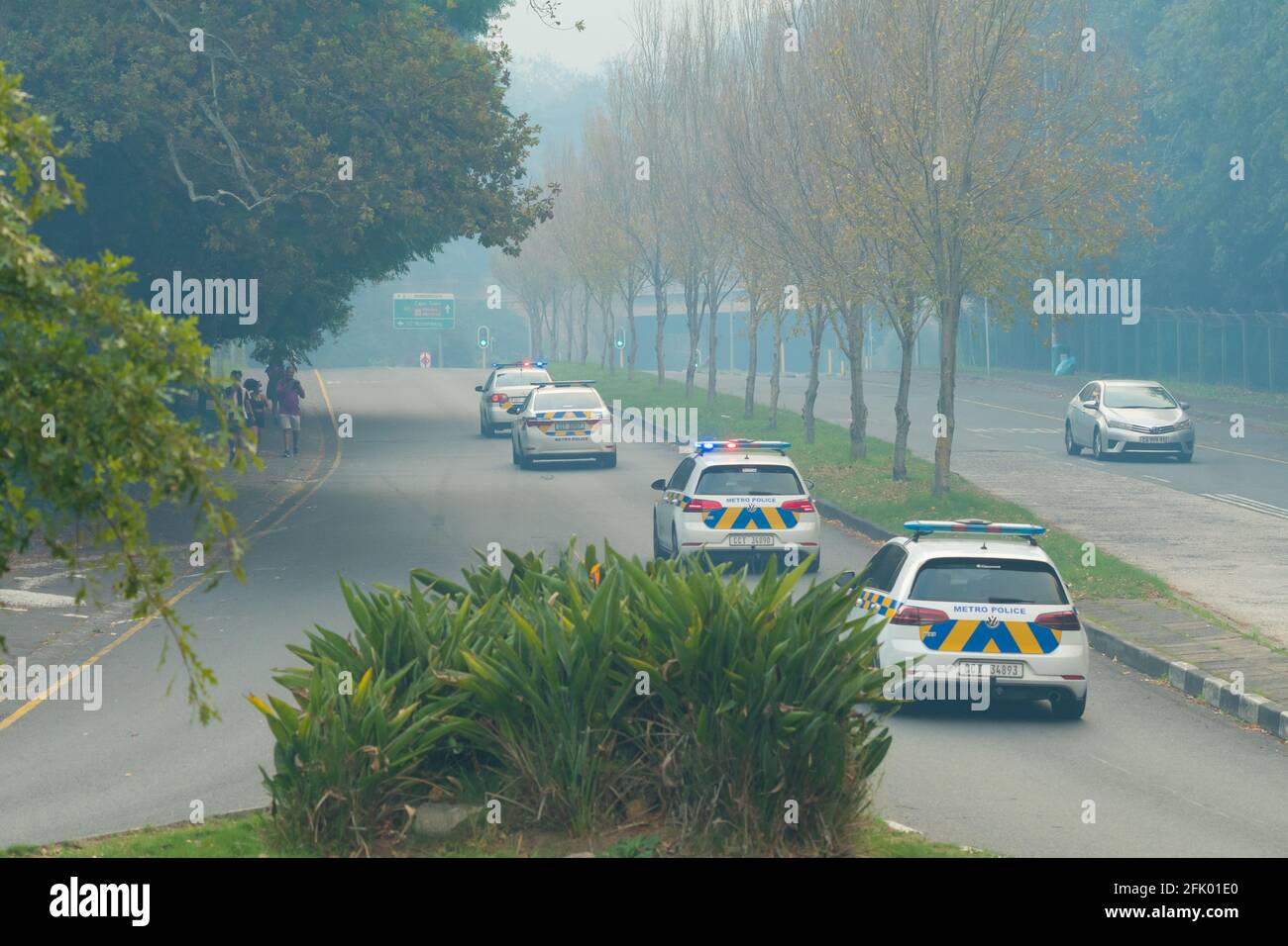 Metro police patrol cars or vehicles drive up a smoke filled road during the Cape Town fire as emergency response unit Stock Photo