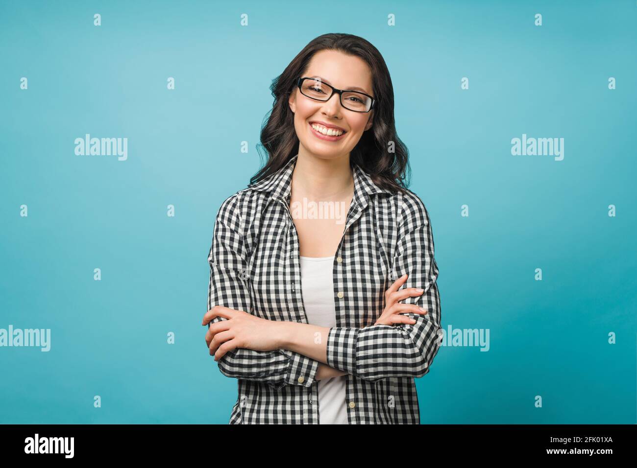 Business portrait of a young woman. A smiling brunette with glasses looks at the camera, her arms crossed over her chest. Stock Photo
