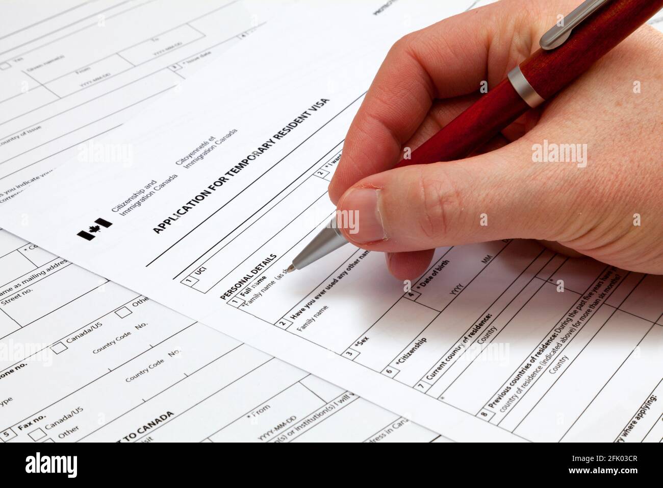 A man holding a ballpoint pen to fill a permanent residence visa  application form to Canada Stock Photo - Alamy