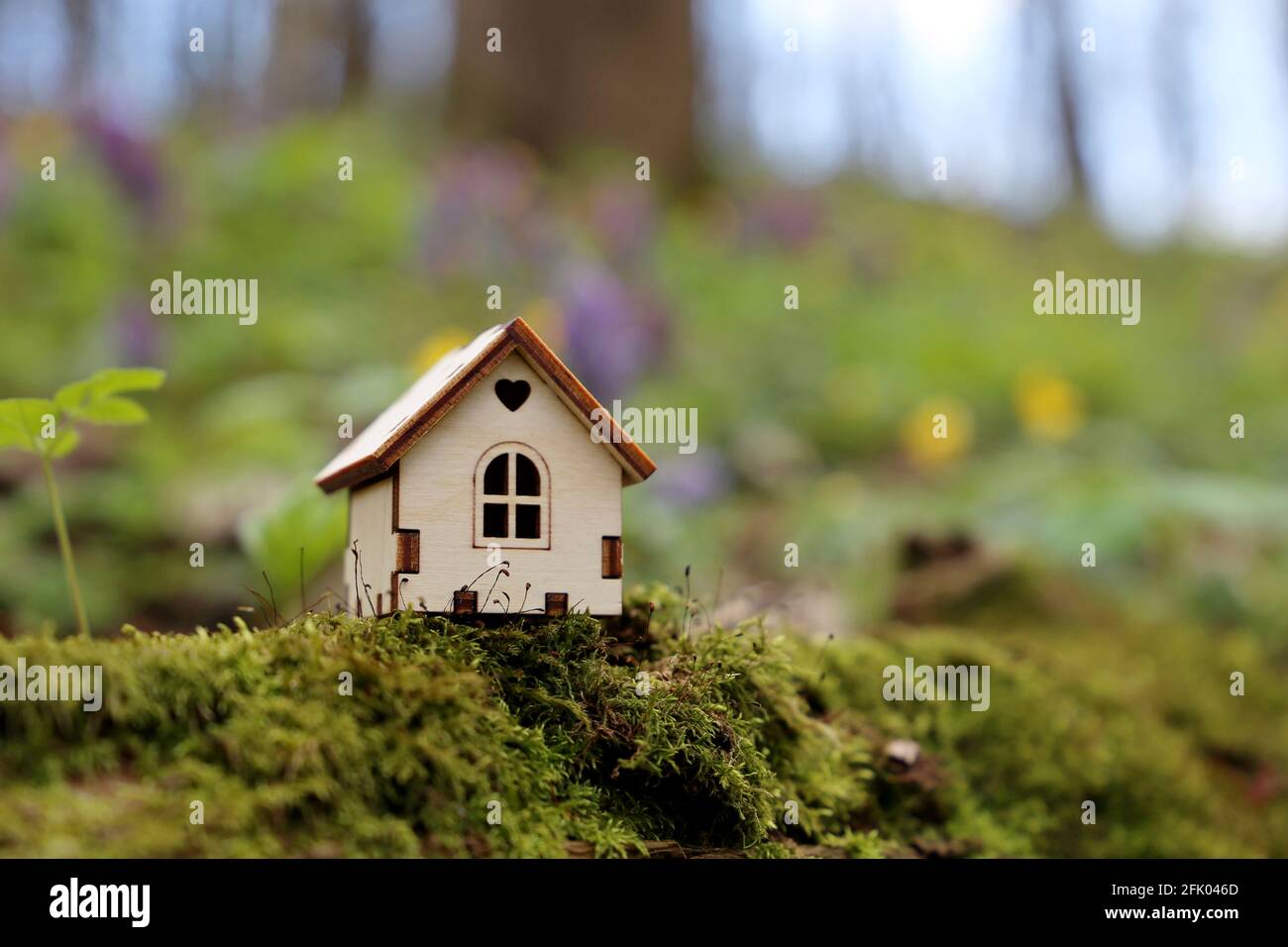 Wooden house model in a forest on spring flowers background. Concept of country cottage, real estate in ecologically clean area, vivid colors of fairy Stock Photo