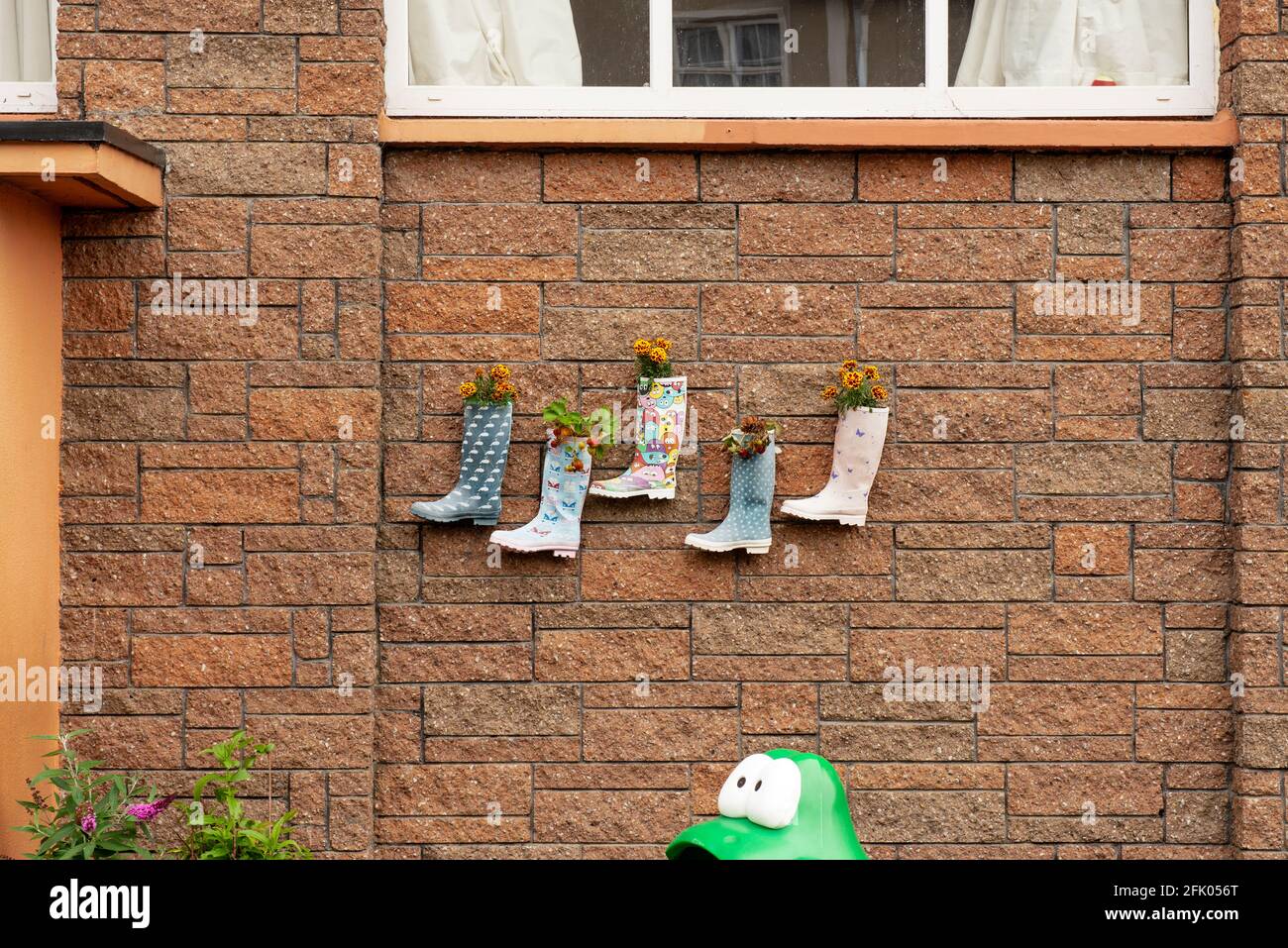 Funny kid's Wellington welly boots plant pots with planted strawberries and flowers hanging on brick wall in kindergarten backyard in Youghal, Ireland Stock Photo
