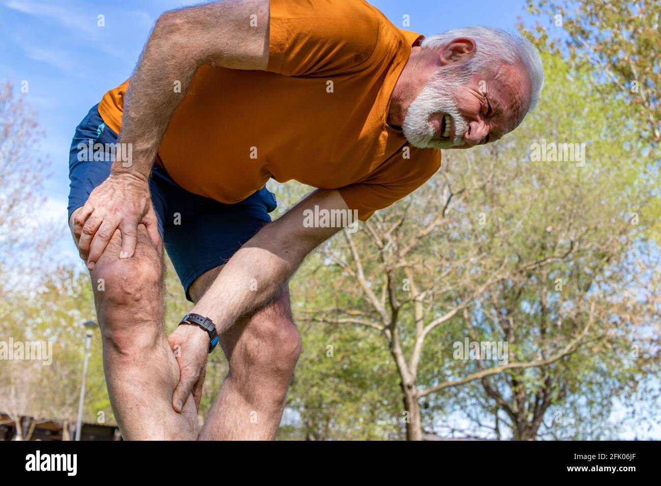 Senior man frowning with muscle pain during training outdoors. Calf leg