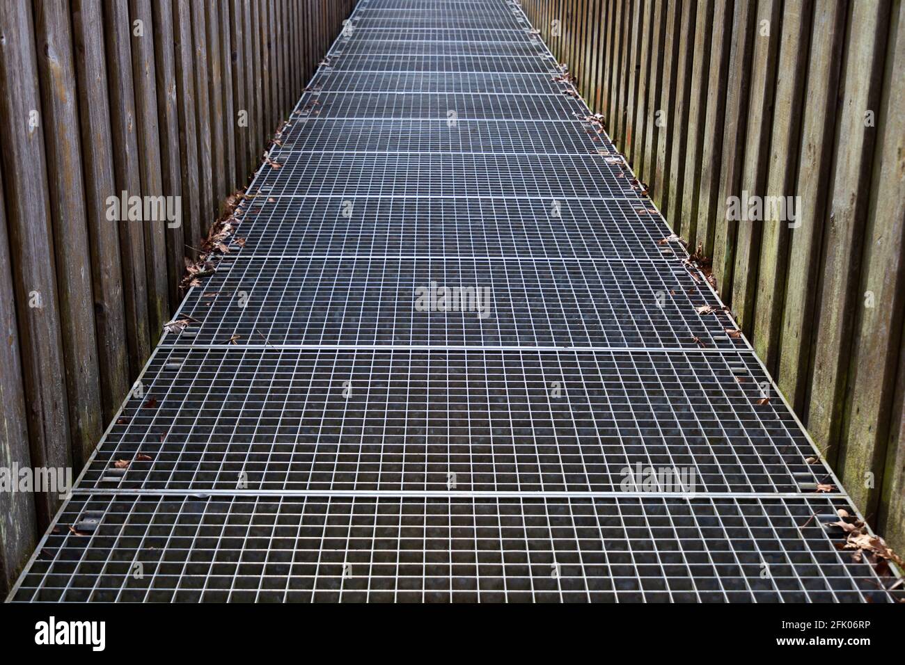 Footbridge with iron grating floor and wooden railing crossing a river Stock Photo