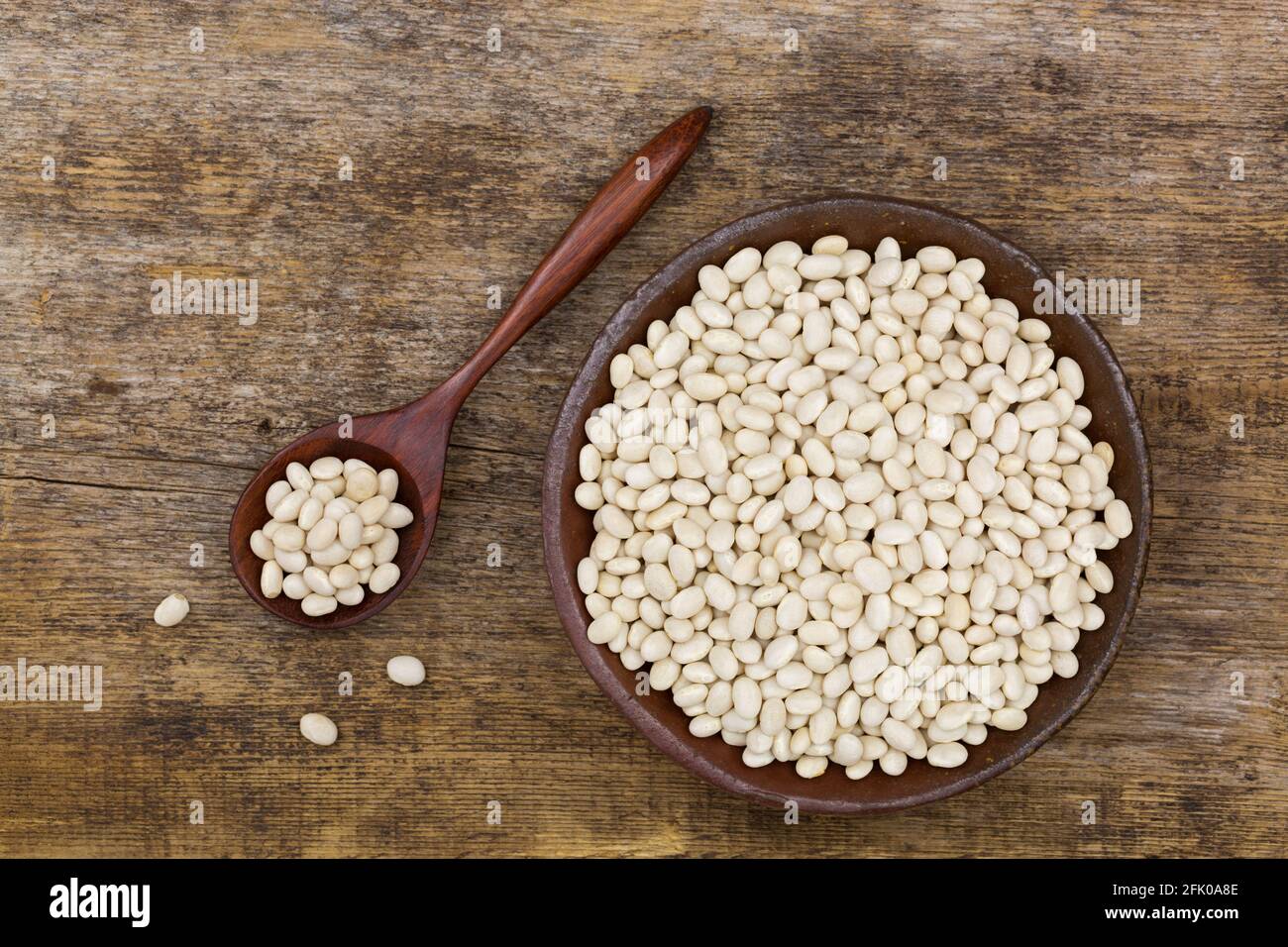 White pea beans, also called Navy bean, Pearl Haricot, Boston bean in clay bowl on wooden background, top view (Phaseolus vulgaris) Stock Photo