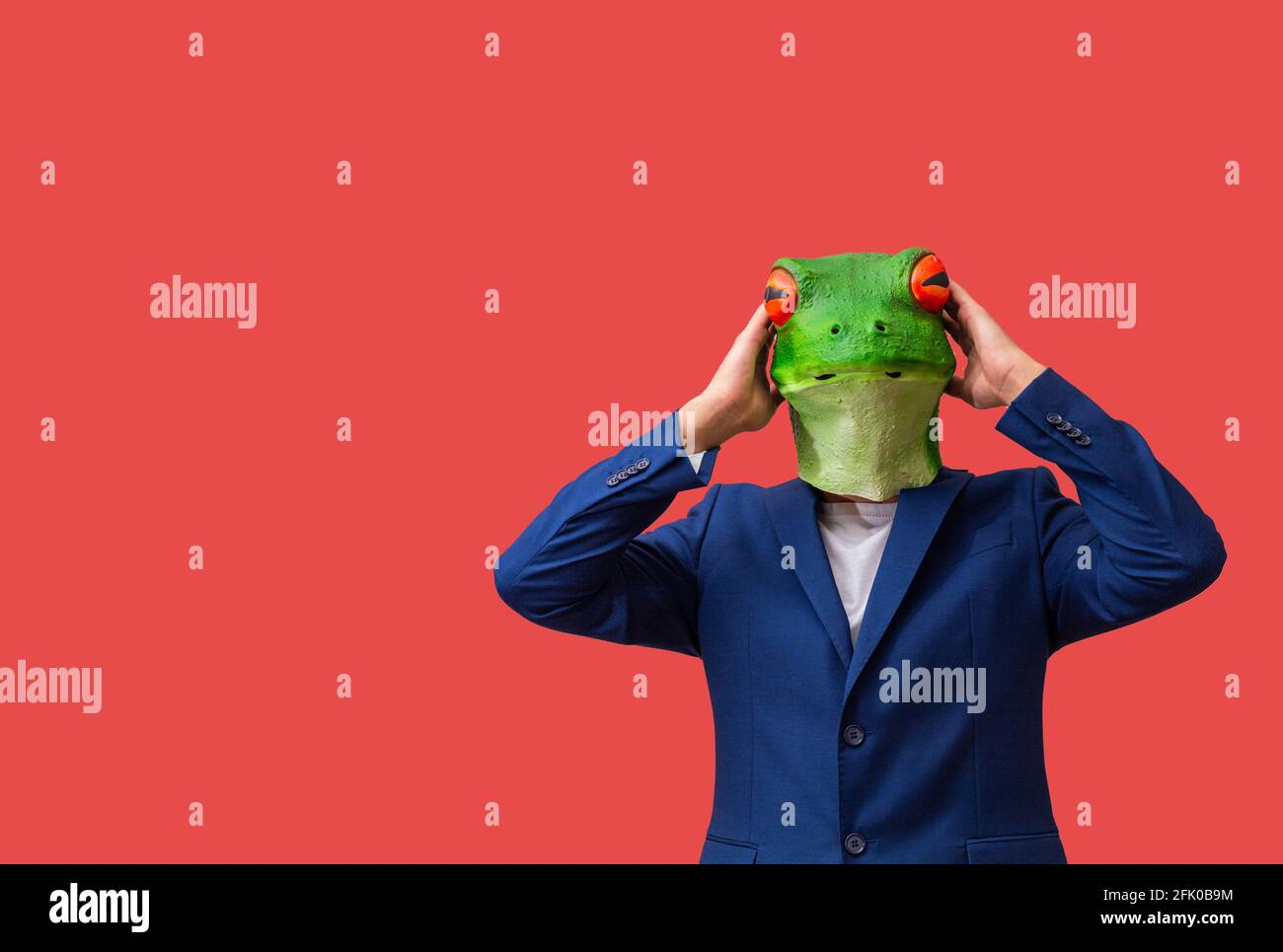 man with googly-eyed frog mask surprised with his hands on his head on red background with copy space Stock Photo