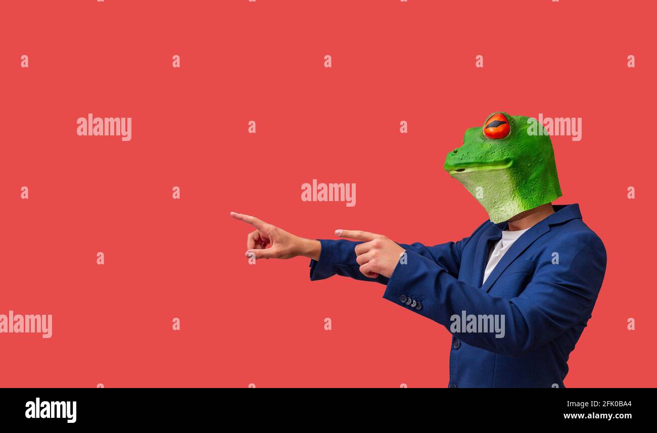 man in frog mask with bulging eyes looking and pointing with both hands on red background with copy space Stock Photo