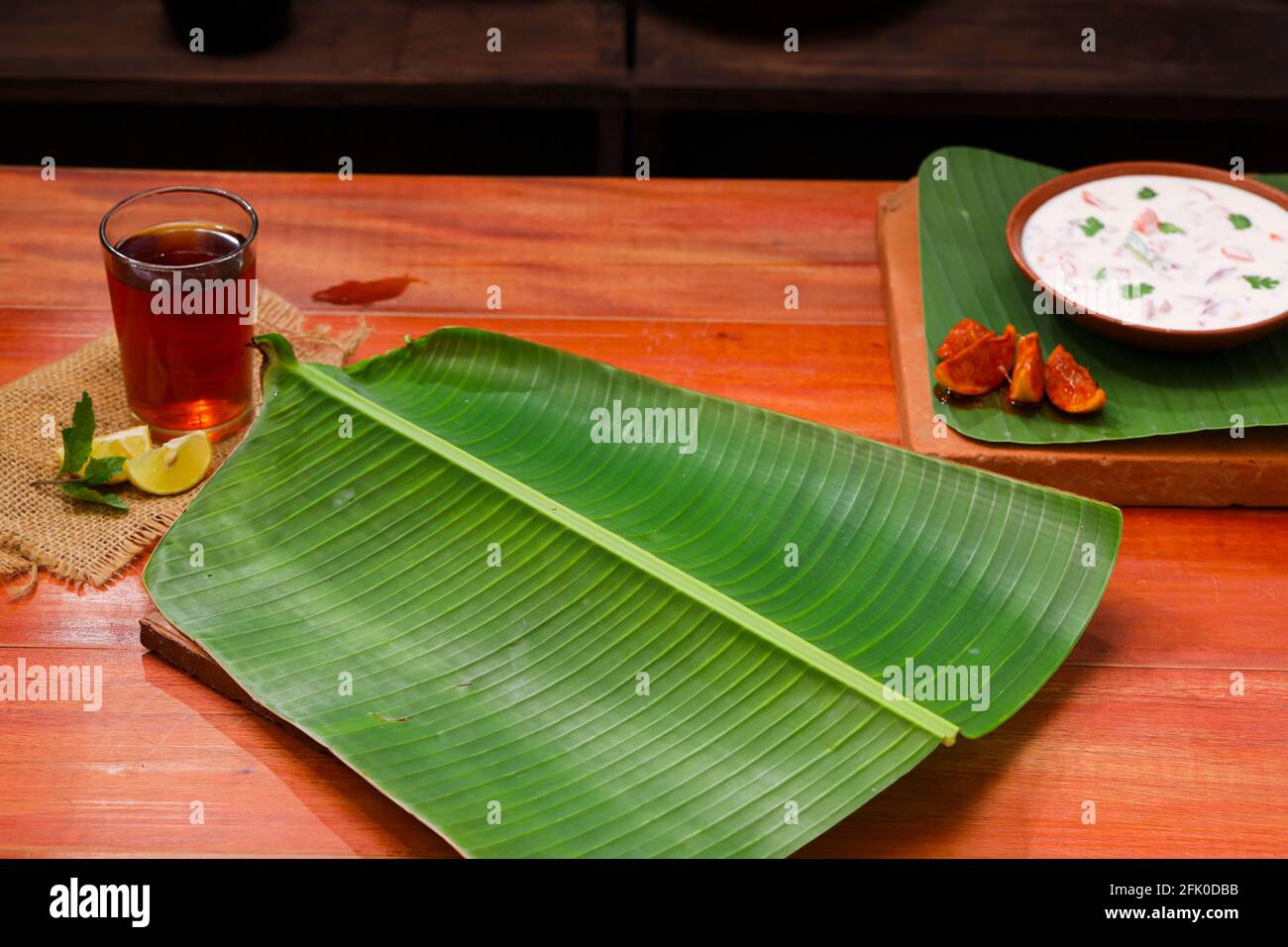 Banana leaf,fresh green banana leaf which is empty placed on wooden texture  with a small bowl of raitha and a glass of lemon tea placed beside it, kit  Stock Photo - Alamy