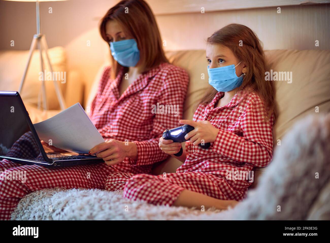 Woman in pajamas with notebook and papers working from home wearing  protective mask while her kid, daughter playing computer console games  Stock Photo - Alamy
