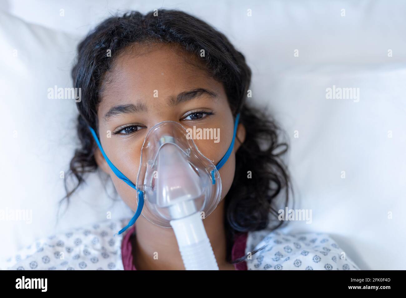 Portrait of sick mixed race girl lying in hospital bed wearing oxygen mask ventilator Stock Photo
