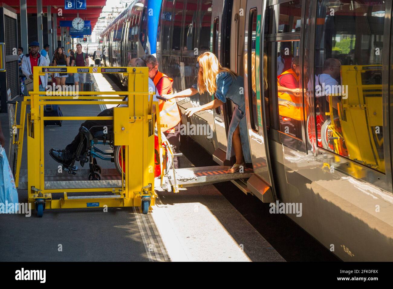 A railway worker provides help to a disabled passenger alighting from