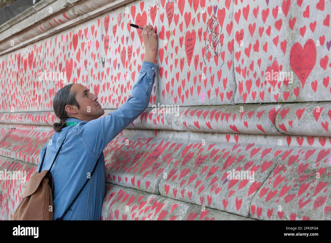 London, UK, 27 April 2021: Clifford Kelly writes on the National Covid Memorial Wall in tribute to his father, George Kelly, who died on 9 January 2021 age 63. Prime Minister Boris Johnson faces allegations he would have let 'bodies pile up'. With one heart drawn for each of the over 150,000 people who died in the UK coronavirus pandemic, the memorial stretches along the wall of St Thomas's Hospital, facing the Houses of Parliament on the opposite bank of the River Thames. Anna Watson/Alamy Live News Stock Photo