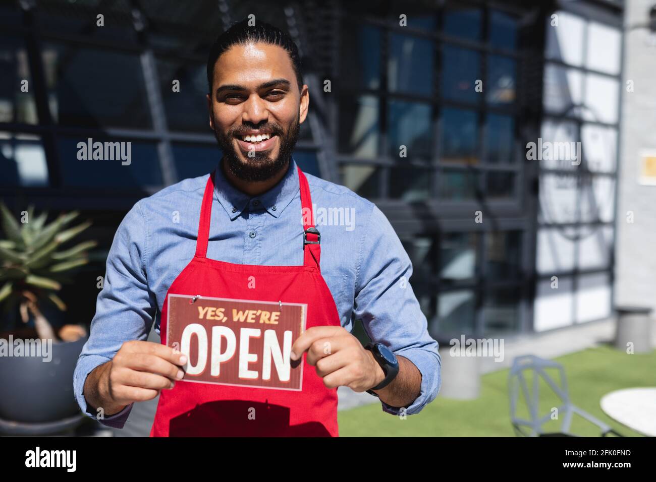 Happy mixed race male waiter holding open sign and looking at camera Stock Photo