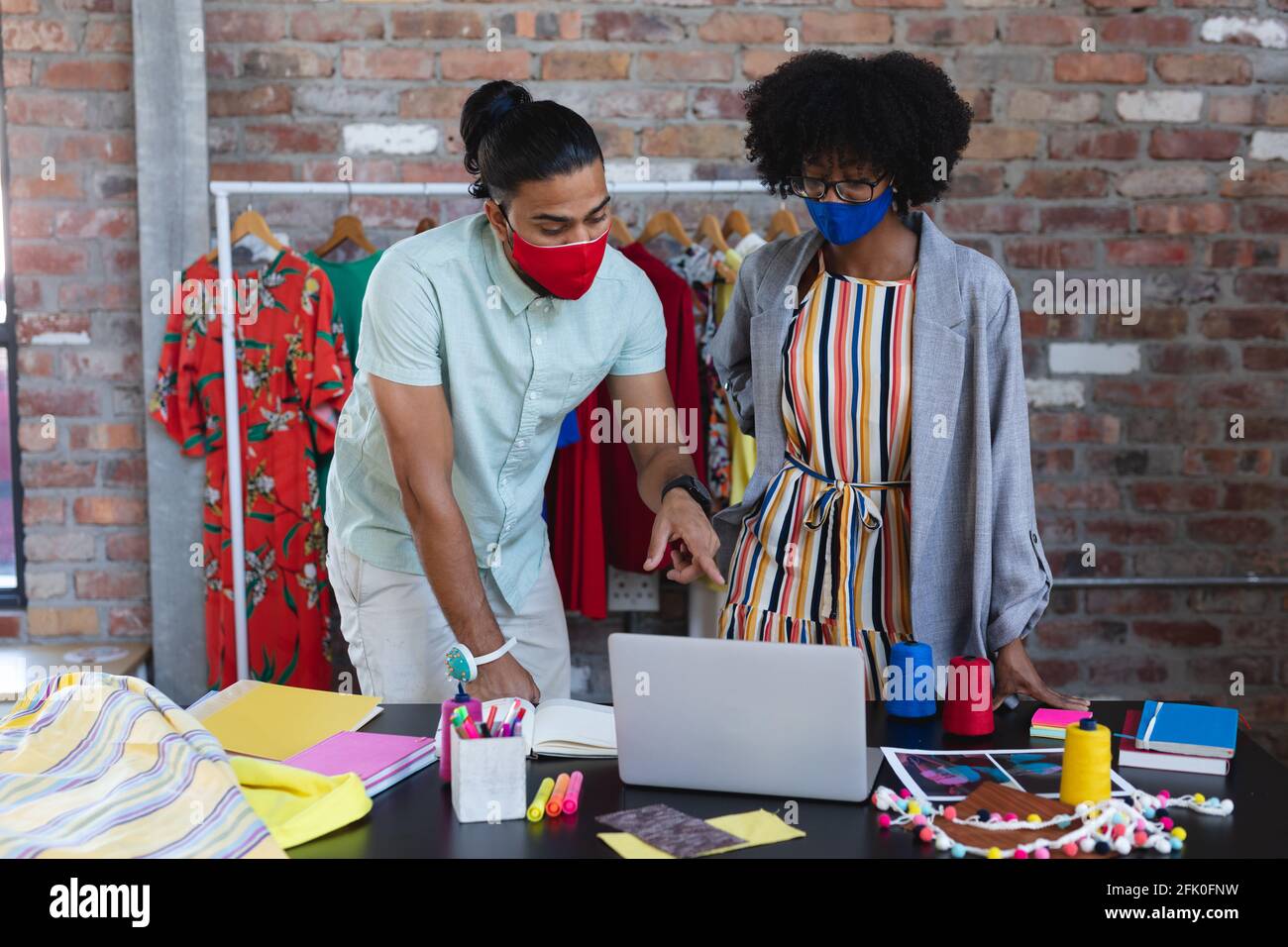 Diverse male and female designers looking at laptop and talking Stock Photo