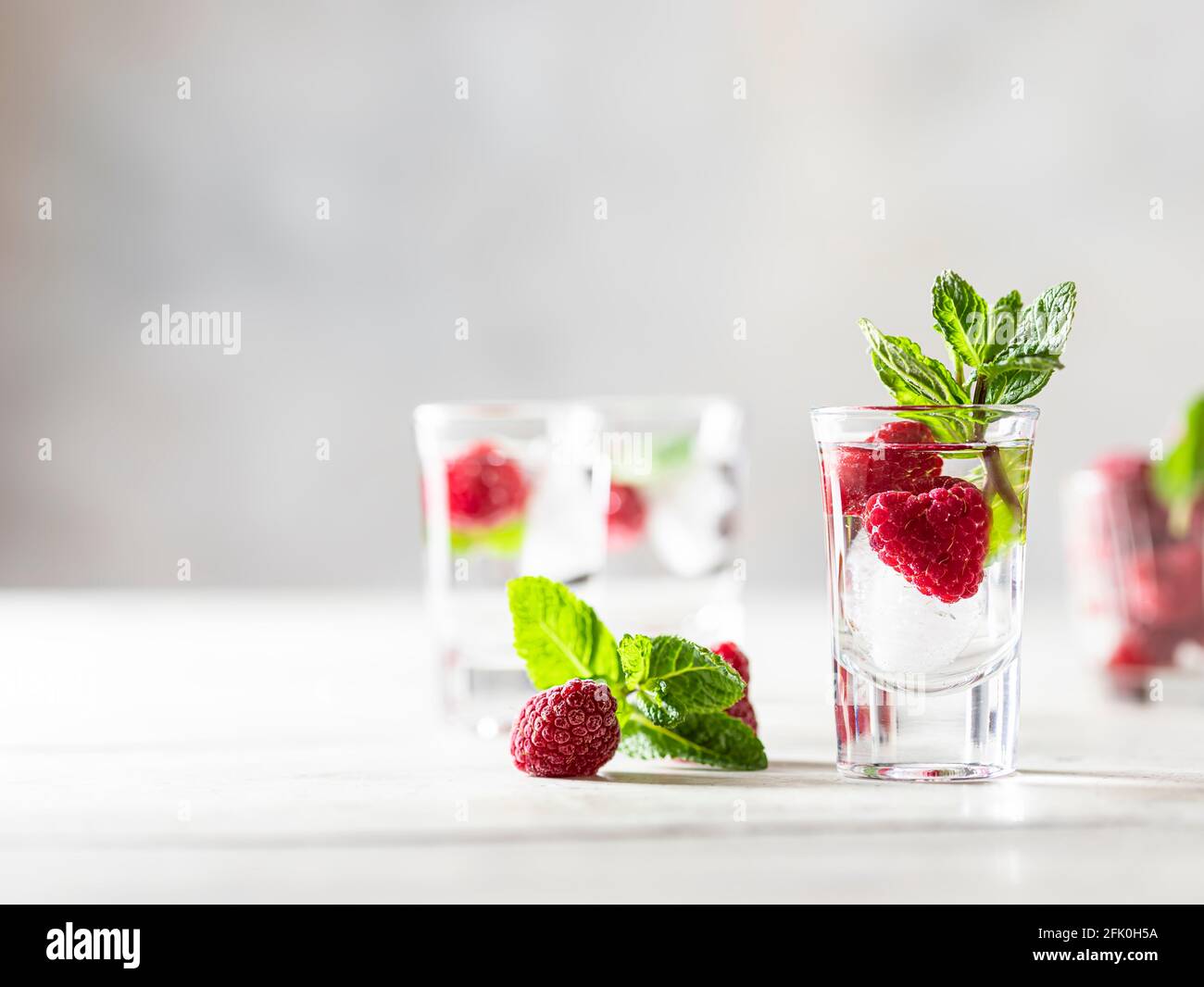 Raspberry vodka glass shot with fruit inside. Fresh summer shots for party. Berries in alcohol glass. Glass of sparkling water. Alcohol shots Stock Photo
