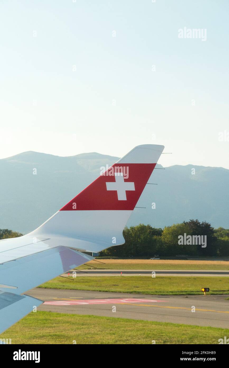 View of plane wing displaying the Swiss logo flag / airplane wing of a  Bombardier C series and the mountainous landscape surrounding Geneva /  Geneve 'Cointrin' Airport, Switzerland. (101 Stock Photo - Alamy