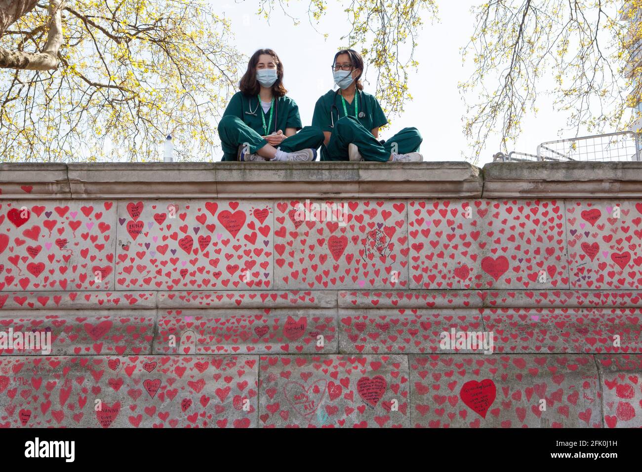 London, UK, 27 April 2021: Student doctors Charlie and Surina take a break sitting above the National Covid Memorial Wall as Prime Minister Boris Johnson still faces accusations of having preferred that 'bodies pile up' rather than have a third lockdown. With one heart drawn for each of the over 150,000 people who died in the UK coronavirus pandemic, the memorial stretches along the wall of St Thomas's Hospital, facing the Houses of Parliament on the opposite bank of the River Thames. Anna Watson/Alamy Live News Stock Photo