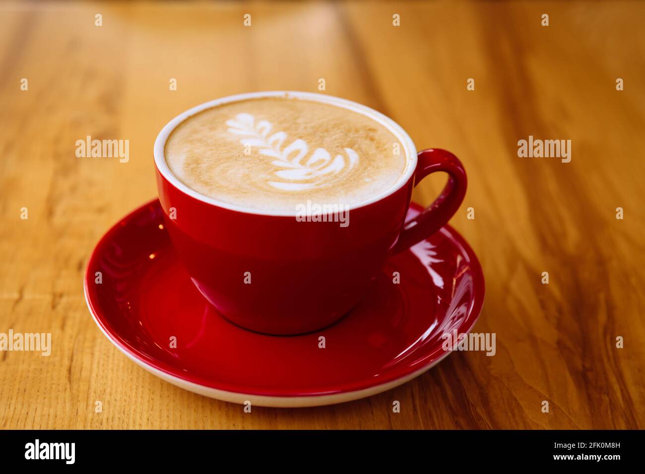 Aromatic coffee in a red cup with milk foam and latte art on a light wooden table. Stock Photo