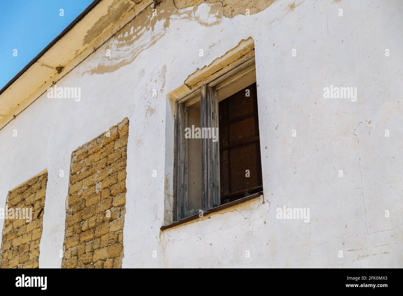 An old wall of an abandoned crumbling house with a boarded-up window and laid bricks. Stock Photo