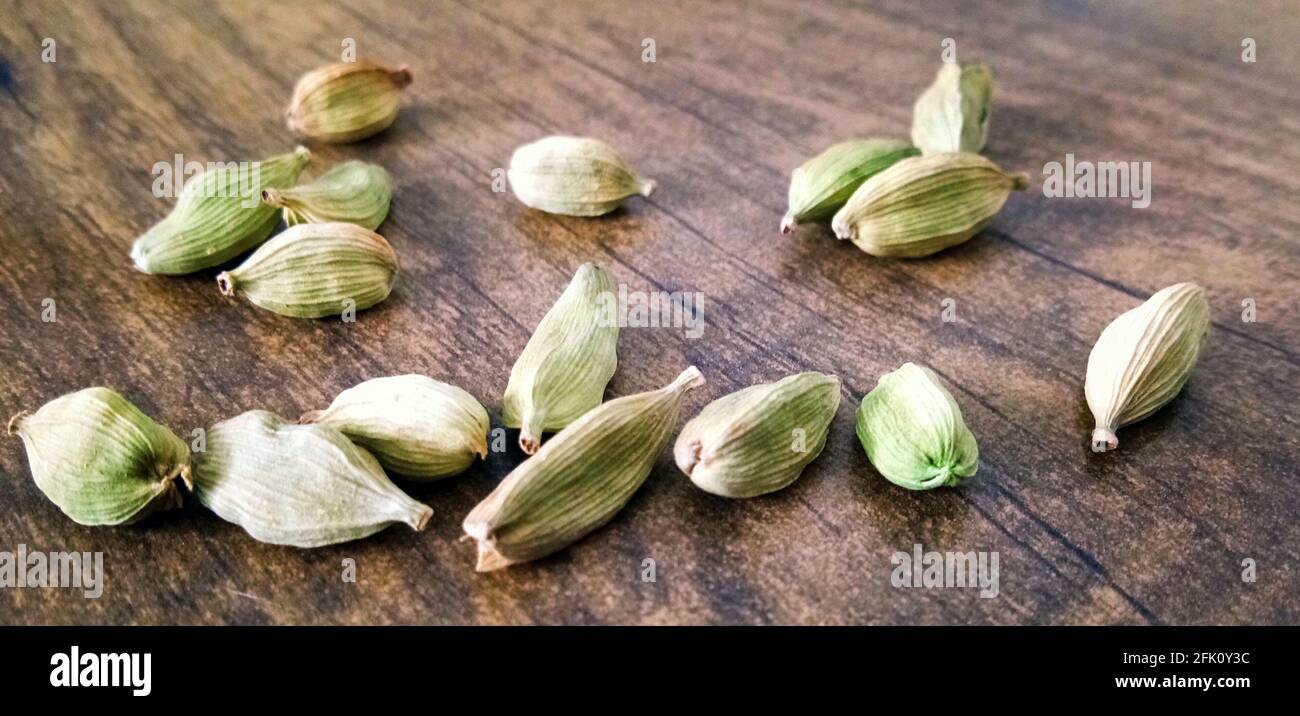 Closeup top view of dried green Elettaria cardamomum fruits with seeds, cardamom spice scattered on wooden background Stock Photo