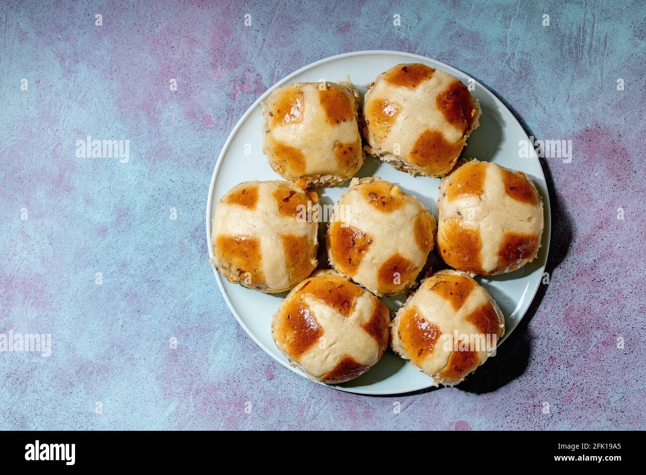 Homemade Easter traditional hot cross buns on ceramic plate over blue texture background. Flat lay, space Stock Photo