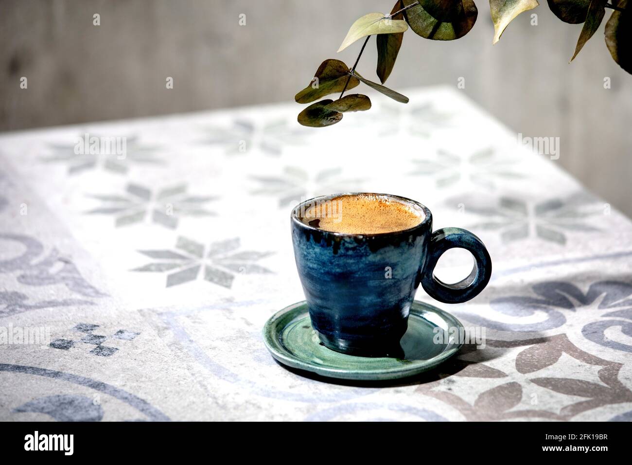 Cup of turkish black frothy coffee on ornate ceramic table with Eucalyptus branches. Sunlight Stock Photo