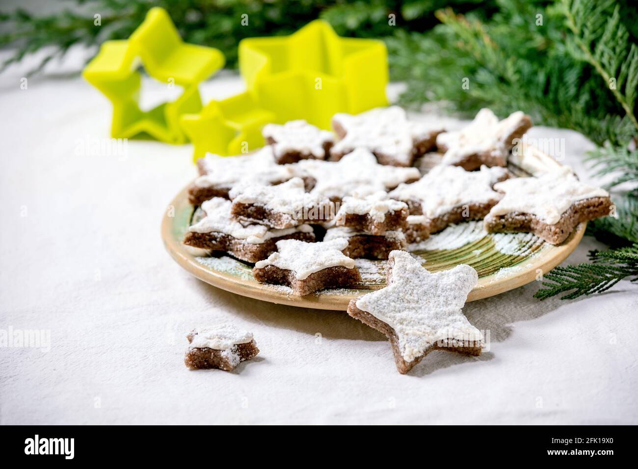 Homemade star shape cocoa almond cookies with white glaze and icing sugar. On ceramic plate with xmas stars cookies cutters, thuja branches, decoratio Stock Photo
