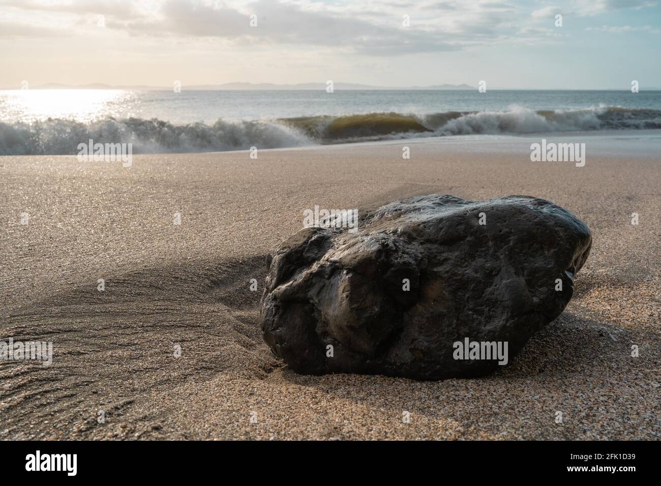 PANAMá, PANAMA - Apr 25, 2021: Rock laying on the sand of a beach on a sunset, waves hitting the beach on the blue sky Stock Photo