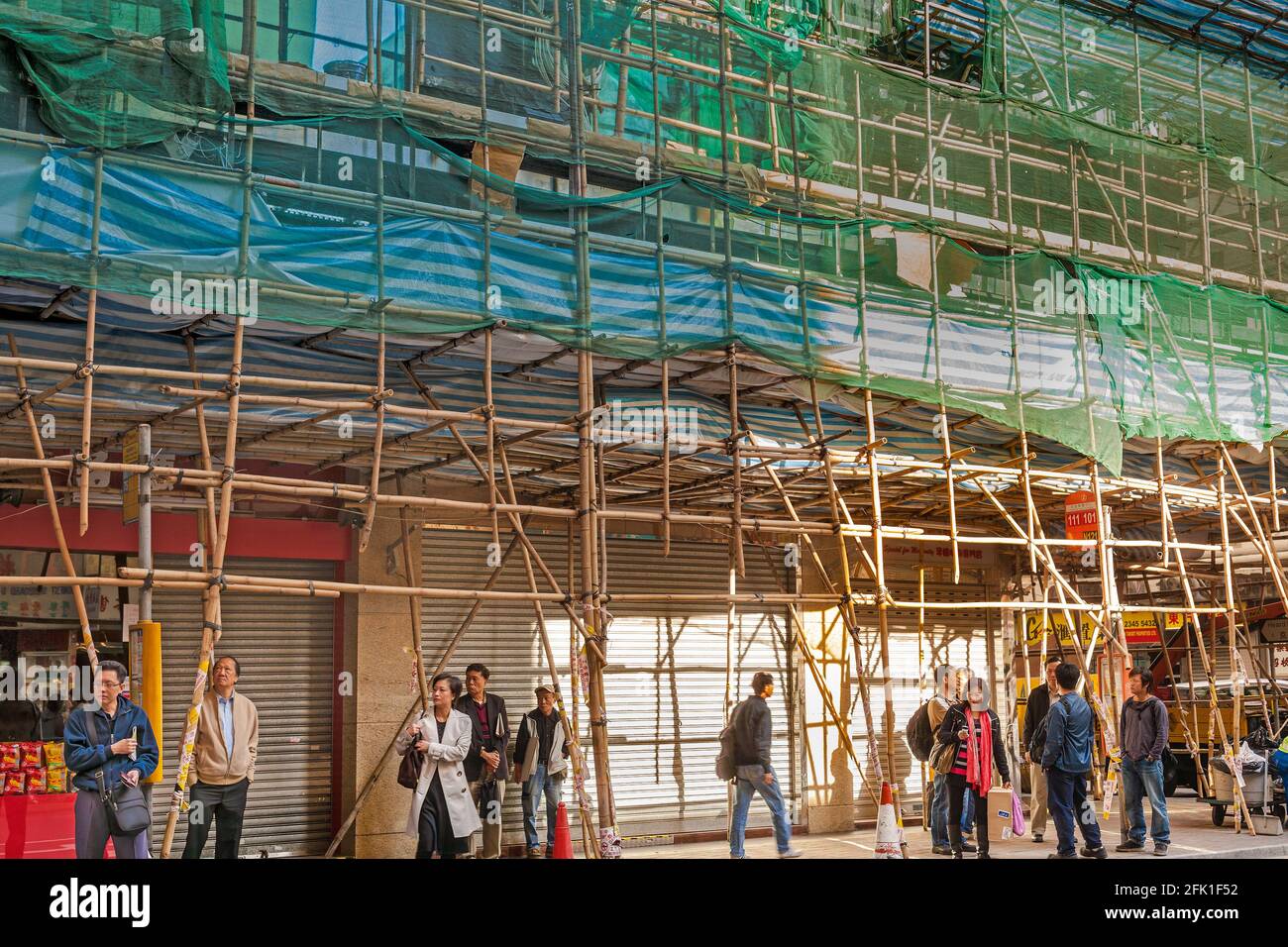 Hong Kong, Hong Kong Island, China, Asia - People at a bus stop under a building wrapped in traditional Chinese scaffolding Stock Photo