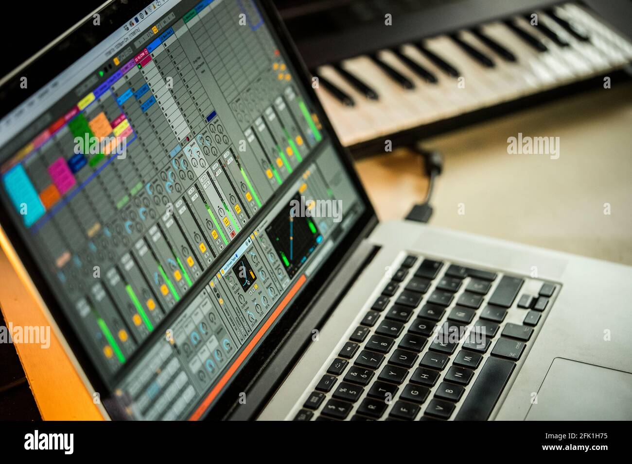 Ableton Live music production software on a macbook pro with synth in background. Stock Photo