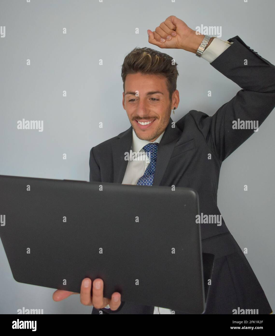 Young Spanish man doing a winner gesture during an online meeting with a laptop in a formal outfit Stock Photo