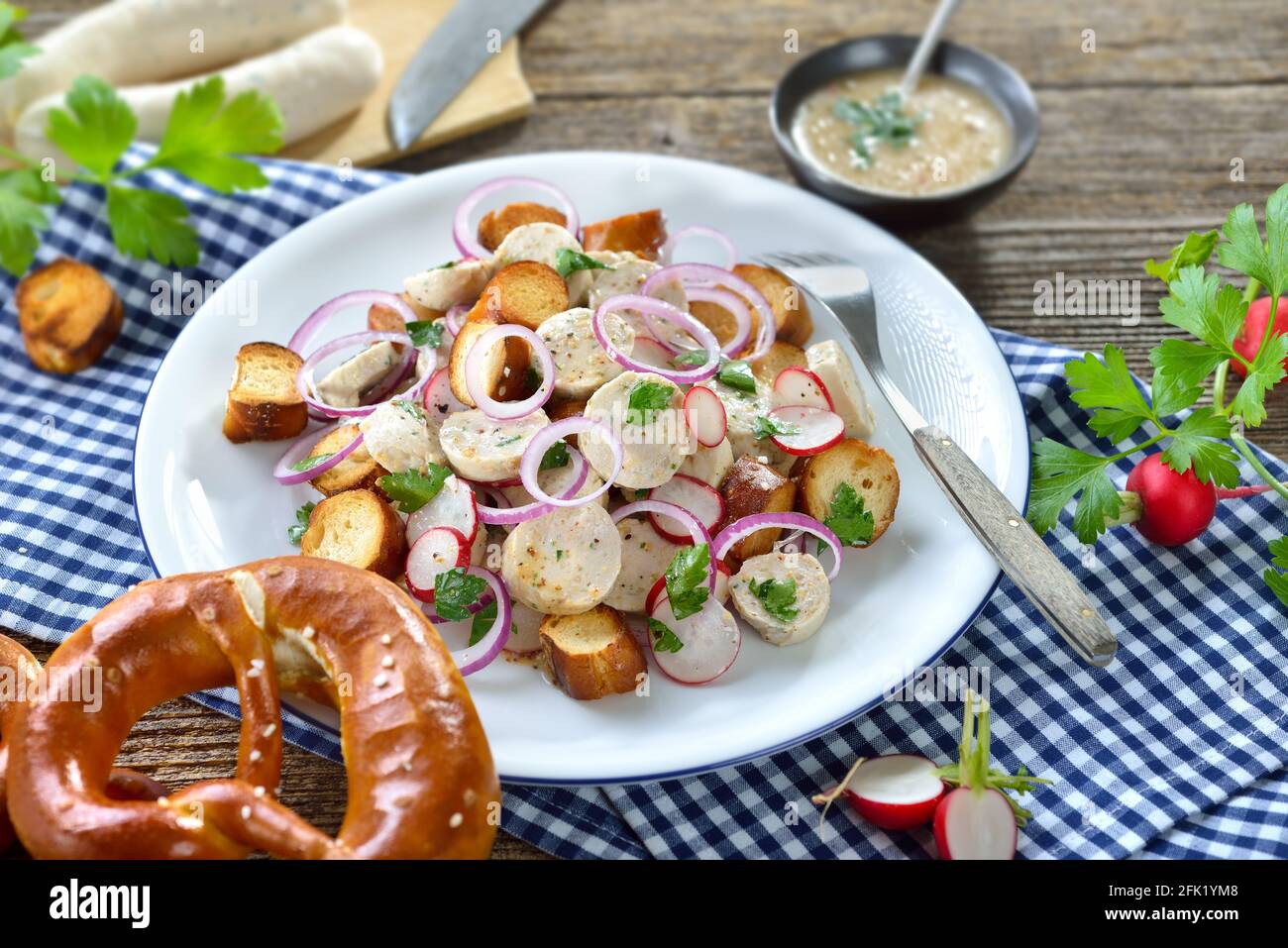 Hearty Bavarian salad with cut veal sausages, roasted pretzel slices and a mustard dressing on a rustic wooden table Stock Photo