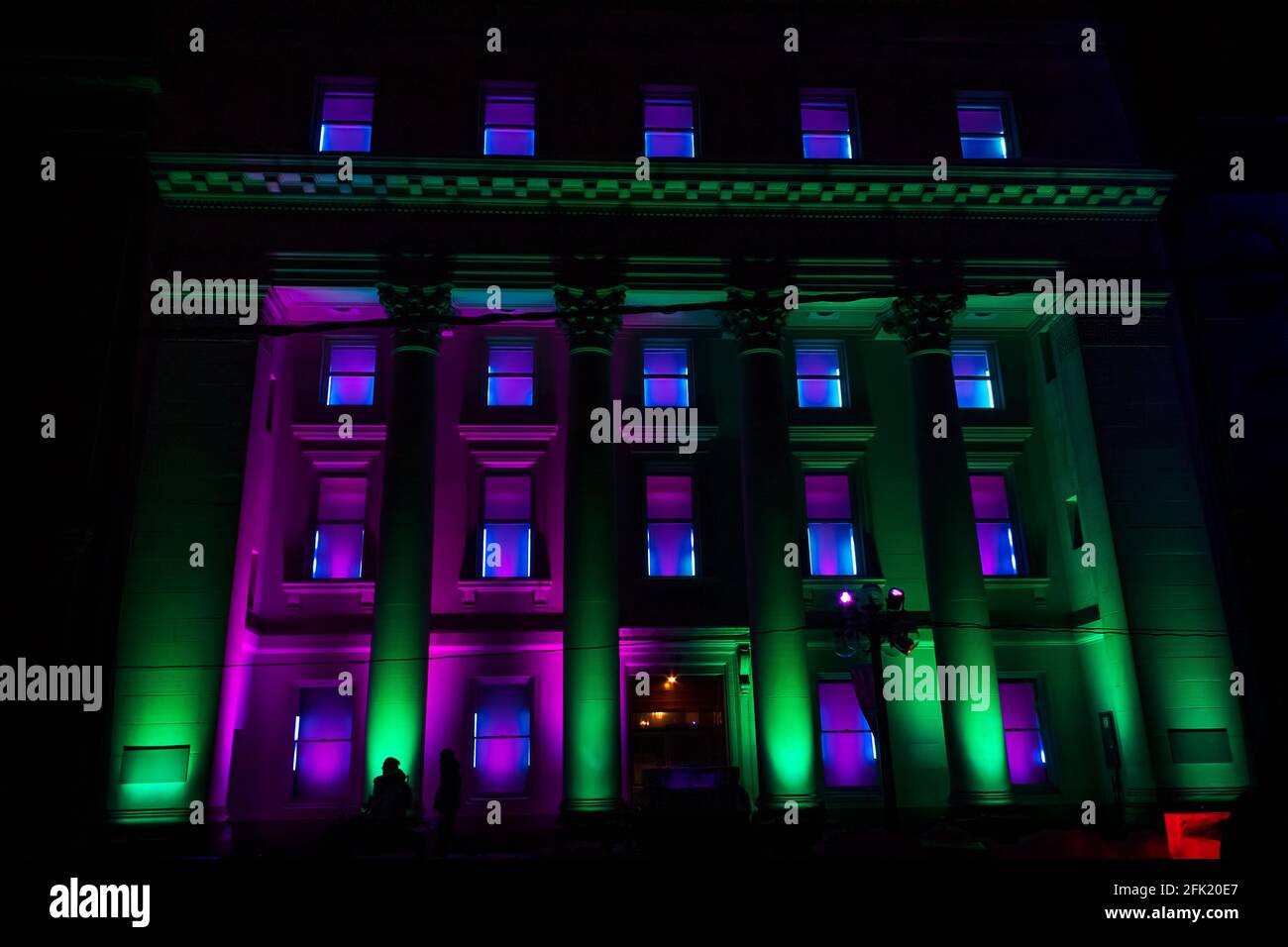 Four-story building with columns illuminated at night with green and purple lights for a winter festival Stock Photo