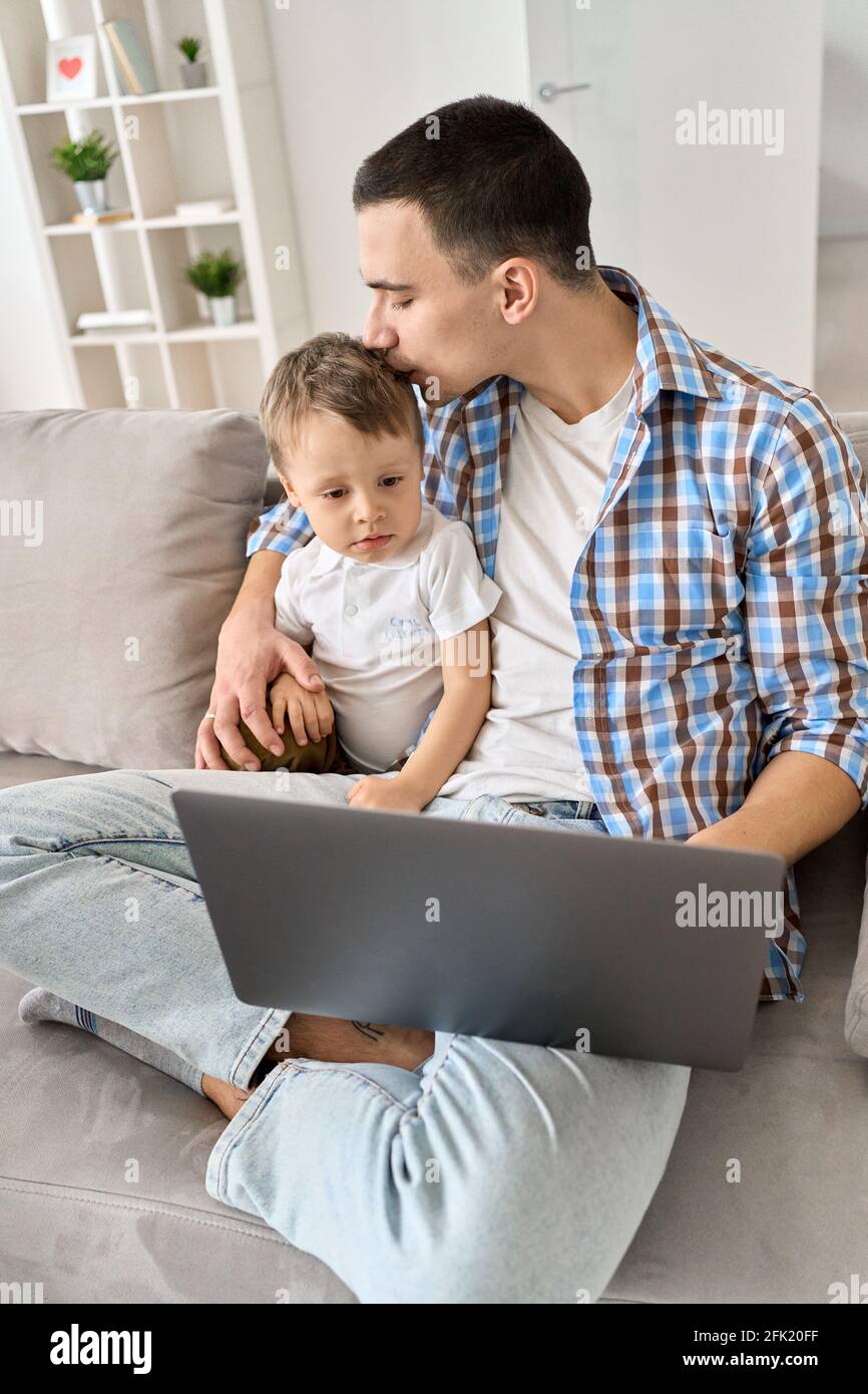 Young dad sitting on sofa at home with kid watching educational classes on pc. Stock Photo