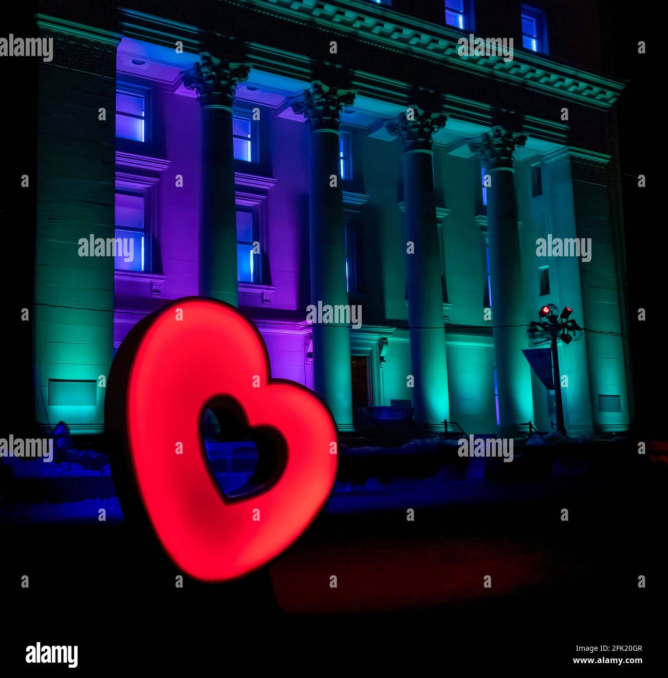 Classical style heritage bank building illuminated with aqua and purple colours at night, with a colour-changing heart in front Stock Photo