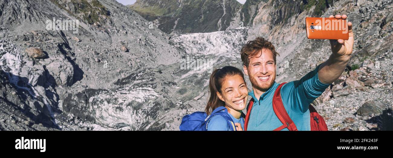 Selfie couple taking phone self-portrait on New Zealand by Franz Josef Glacier. New Zealand tourists smiling happy in nature in Westland Tai Poutini Stock Photo